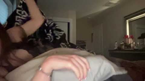 Media: A dimly-lit, blurry video of a woman in a black floral dress hugging a man lying in bed, with a cluttered nightstand in the background.