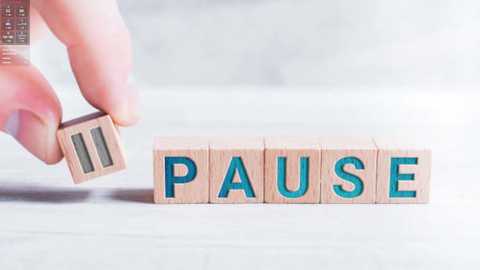 Media: A video depicts a hand holding a wooden letter \"P\" from a block puzzle spelling \"PAUSE,\" set on a light wooden surface. The background is a blurred, light-colored wall.