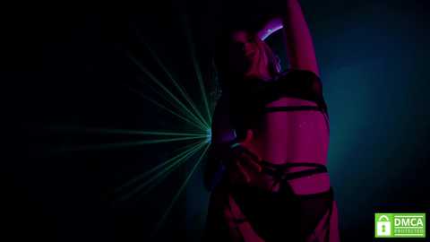 Media: Video of a woman in black bondage gear, arms raised, with a neon green laser beam emanating from her hand against a dark, moody background.