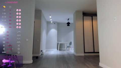 Video of a modern, minimalist bedroom with light grey walls, wooden floor, and a white desk. Black pendant lights hang above the desk, and a grey chair is placed beside it.