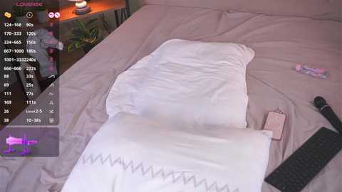 A video of a bedroom with a white pillow on a beige bed, a pink phone, and a black keyboard on the floor. The room has a cozy, minimalist ambiance.