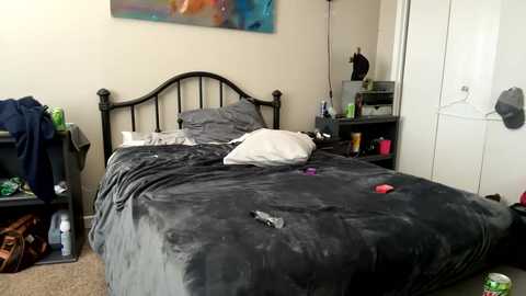 Media: Video of a messy bedroom with a black metal bed covered in gray bedding, a white pillow, and scattered items on the floor.