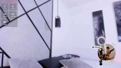 Video of a minimalist, modern bedroom with a white and black color scheme, featuring geometric shapes and a hanging lamp. A video game screen overlay shows a suggestive scene.