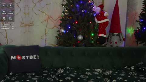 Media: A video of a cozy living room with a green velvet sofa, a decorated Christmas tree, and a red Santa Claus figurine, adorned with colorful lights and a dark pillow with \"MST3K\" text.