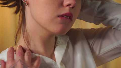 Media: Video of a Caucasian woman with fair skin, brown hair, and red lipstick, adjusting her collar, wearing a white button-down shirt, in a beige background.