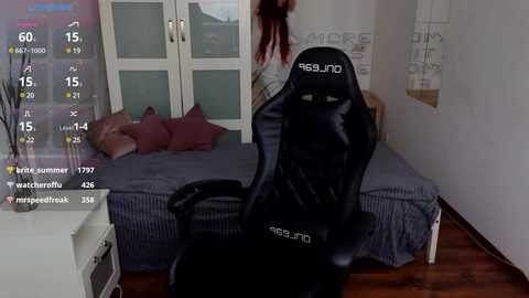 Video of a modern bedroom with a black gaming chair facing a purple-striped bed. Background includes a white wall with a decorative poster and a white nightstand.