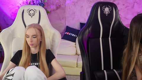 Media: Video of two young women in black \"Stress\" T-shirts, seated in white and black gaming chairs with skull logos, against a purple-lit, rustic brick wall background.