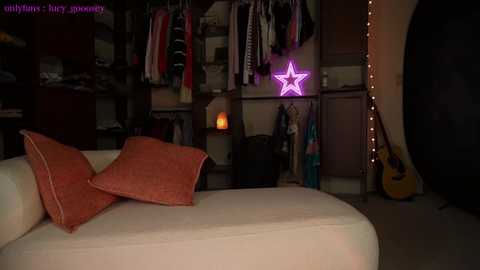 A dimly lit video of a cozy living room with a white sofa, orange throw pillows, a glowing star-shaped neon light, and an acoustic guitar, with a dark background and warm, ambient lighting.