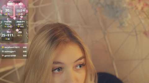 Media: Video of a young woman with long blonde hair, wearing makeup, gazing intently at a smartphone screen displaying a game with hearts and coins.