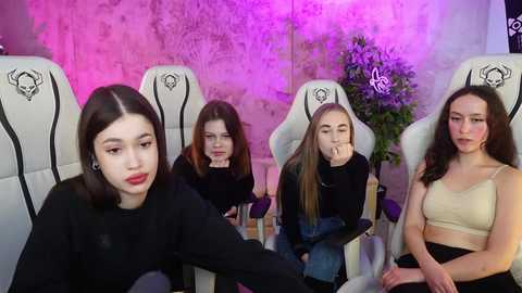 Video of five young women with pale skin and dark hair, sitting in white gaming chairs, wearing casual clothes, under purple lighting, looking bored and resting their heads.