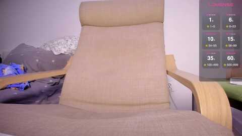 Video of a beige, cushioned recliner chair in a messy bedroom with blue sheets, a white pillow, and a digital display showing \"Fitness\" stats on the right wall.