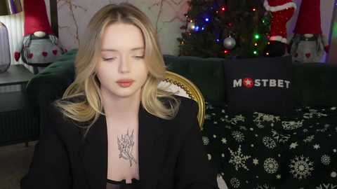 Media: A video of a young woman with blonde hair, wearing a black blazer, sitting in a cozy living room with a decorated Christmas tree, a \"MostBet\" box, and festive lights in the background.