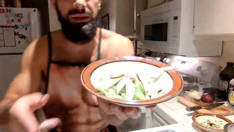 Media: Video of a bearded, shirtless man holding a bowl of stir-fried vegetables in a modern kitchen. Background includes white cabinets, a microwave, and a refrigerator.