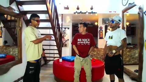 Media: Video of three young men in casual attire, standing in a modern living room with a spiral staircase, red beanbags, and a wooden floor.