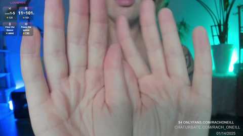 Media: A close-up video of a person's hands covering their mouth, taken in a dimly lit room with a greenish-blue hue. The background features a potted plant and a digital clock.