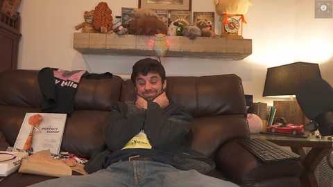 Media: A video of a man lounging on a brown leather sofa, wearing a dark jacket and jeans, surrounded by plush toys and a lamp.