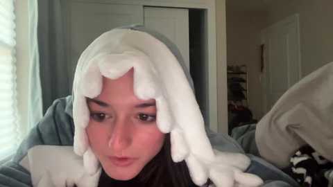 Media: A video of a person wearing a white, fluffy wig resembling octopus tentacles, with a serious expression. The background shows a dimly lit room with closed doors and a window.