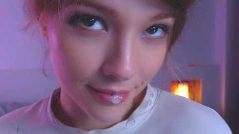 Media: Video of a young Asian woman with light skin and brown eyes, wearing a white top. She has a slight smile, with a small amount of drool on her lip. Background shows a dimly lit room with a soft purple hue.