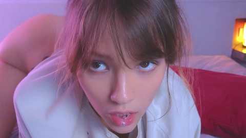 Media: A video shows a young Asian woman with fair skin and straight brown hair, leaning forward with a seductive expression. She wears a white shirt. Background includes a red bed and a lit candle.