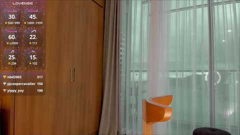 Media: Video of a modern bedroom with wooden wardrobe, white curtains, and a bright orange chair; a digital screen displaying weather and temperature information is visible in the background.