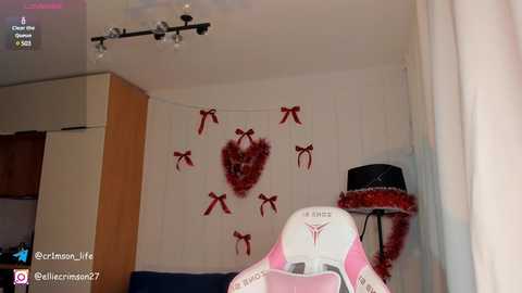 Media: A video of a cozy, festive room with white walls, a red heart-shaped wreath, and a black lamp with a pink and white chair.