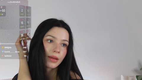 Media: Video of a young woman with long black hair and light skin, wearing a black top, holding a smartphone in her left hand, displaying a digital calendar with various dates and events.