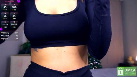 Media: Video of a woman with light skin, wearing a black sports bra and black pants, with a tattoo on her left side, in a dimly lit room with a Christmas tree in the background.