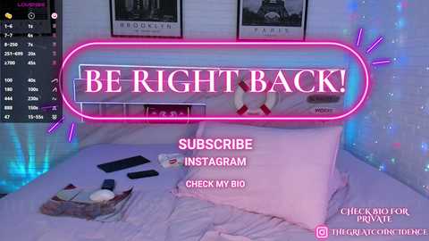 Media: Video of a bedroom with a neon pink sign reading \"BE RIGHT BACK\" in a minimalist, white and grey decor, featuring a bed with scattered clothes and a phone.