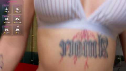 Media: A close-up video of a person's torso, showing a white ribbed bra and a tattoo of \"sorority\" with blood dripping. Background includes a smartphone screen displaying exercise stats and a blurred indoor setting.