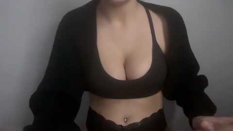 Media: Video of a light-skinned woman with medium-sized breasts, wearing a black bra and black lace panties, with a black cardigan draped over her shoulders. Background is a plain, light-colored wall.