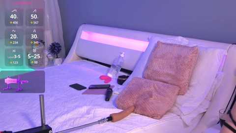 Media: Video of a modern, dimly-lit bedroom with a white bed, a pink pillow, and a laptop; a phone, water bottle, and a knife are on the bed.