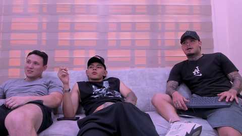 Media: Video of three Asian men, one with tattoos, in casual attire, sitting on a couch in a room with white blinds, holding cigarettes and a laptop.