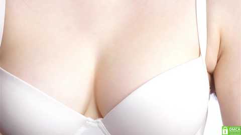 Media: Video of a woman's cleavage in a white bra, with smooth, fair skin and a slight tan line.