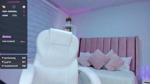 A video of a modern, pink and white bedroom with a plush white recliner chair, a tufted pink headboard, and soft pillows. A live stream screen displays statistics on the left.