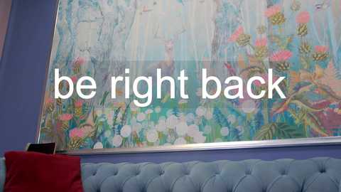 Media: Video of a room with a large, colorful floral painting on a lavender wall. Text reads \"be right back\" in white letters. A light blue tufted sofa and red pillow are visible.