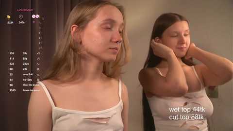 Media: Video of a young woman with long brown hair, wearing a white tank top, adjusting her bra straps, standing in a bedroom with dark curtains, text overlay.