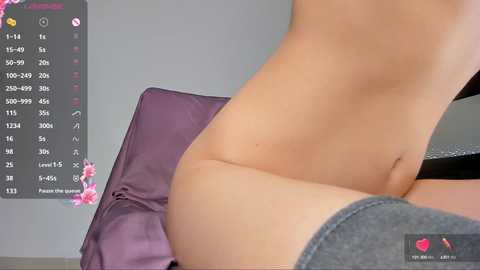 Media: A video of a nude, light-skinned woman with a slender physique, wearing only dark gray thigh-high socks, sitting on a purple cushion against a grey wall. The image includes a digital clock with pink flowers and a text prompt.