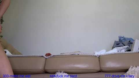 Media: A video depicts a beige leather couch with a white cushion, partially covered by a man\u2019s lower torso, partially visible. Text overlays the image, stating \"3333 mean me\" and \"7777 fuck me hard.\