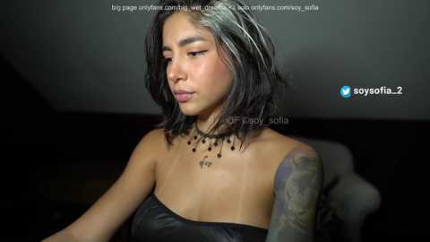 Media: Video of a young Asian woman with medium-length, wet, black hair, wearing a strapless black leather dress and black choker with small black beads. She has a tattoo on her right shoulder.