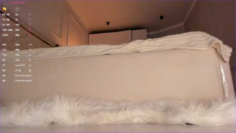 Media: A video of a minimalist bedroom with a white bed covered in fluffy, white faux fur, set against a beige wall. The room has a cozy, serene ambiance.