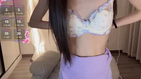 Media: Video of an Asian woman with long black hair, wearing a white lace bra and purple skirt, standing in a modern bedroom with a calendar and floral decorations.