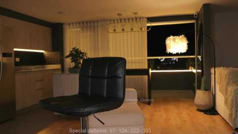 Media: Video of a modern living room with a black leather chair, light wooden flooring, beige curtains, and a chandelier, featuring a contemporary design.