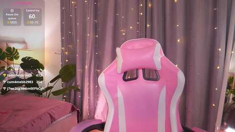 Media: Video of a pink gaming chair with white accents, placed in a cozy room with pastel-colored walls, green plants, and string lights.