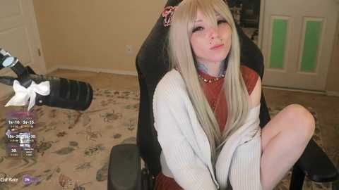 Media: A video of a young woman with long blonde hair, wearing a white and brown sweater, sitting on a gaming chair in a cluttered room with a beige carpet and a door.