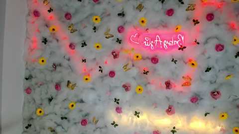 Media: Video of a white marble wall adorned with colorful artificial flowers in yellow, pink, and purple. A neon pink \"EtsyArtist\" logo is prominently displayed in the center.