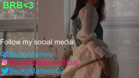 Media: Video of a woman in a white dress, partially blurred, with text overlay promoting social media accounts, set in a softly lit room.