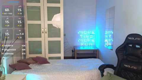 Media: Video of a modern bedroom with a white bed, beige pillows, a large wardrobe, and a \"More Than a Gamer\" neon sign on the wall.