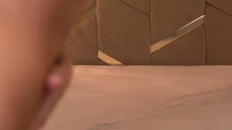 Media: Video of a close-up view of a person's arm, with a geometric, gold-hued, diamond-patterned wall in the background. The skin tone is light, and the texture of the wall appears smooth and metallic.