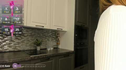 Media: Video of a modern kitchen with white cabinets, a gray and silver mosaic backsplash, a white sweater-wearing woman, and a digital fitness app overlay showing calorie burn.