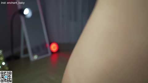 A close-up video of a nude person's thigh and lower abdomen, featuring a red light in the background, taken indoors, with a watermark and QR code in the bottom left corner.